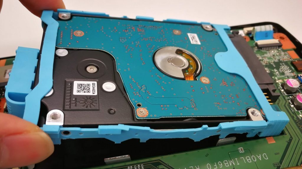 RAIDデータ復旧のためにノートパソコンから取り出された、青い保護フレームに装着された2.5インチの内蔵ハードディスク。