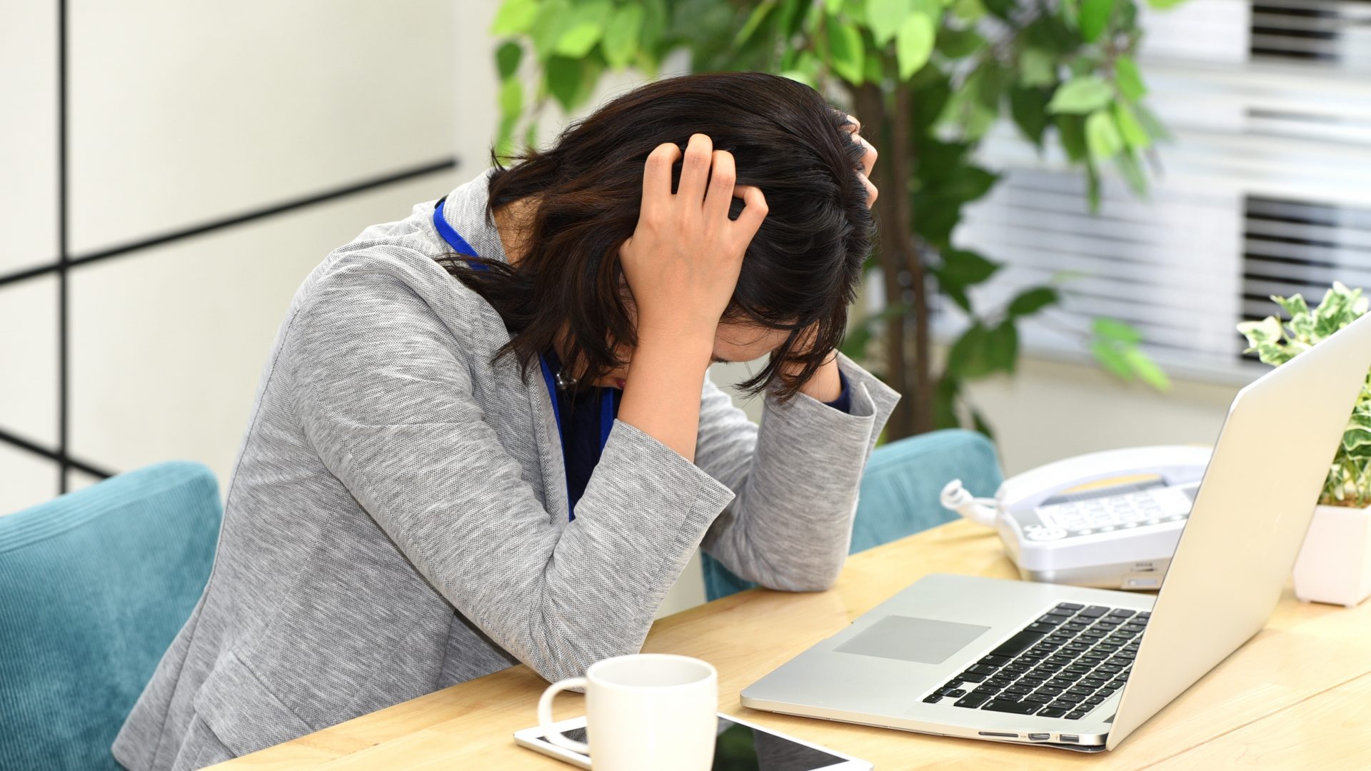 自分のミスでサーバー障害が発生し、データ損失に不安を感じて頭を抱え込む女性。