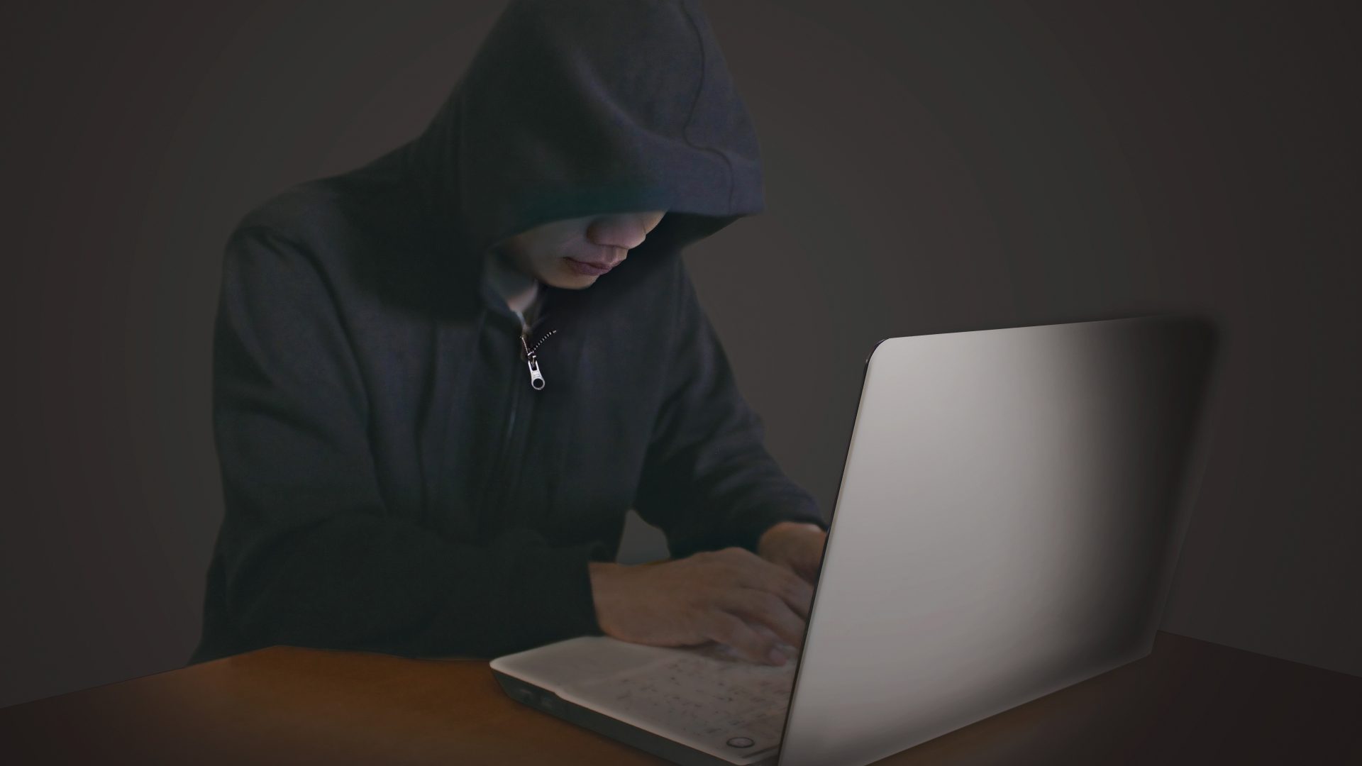 不正なハッキングやサイバー攻撃によるサーバー障害、データ復旧の緊急性を暗示する、暗闇でPCを操作するフードの人物。