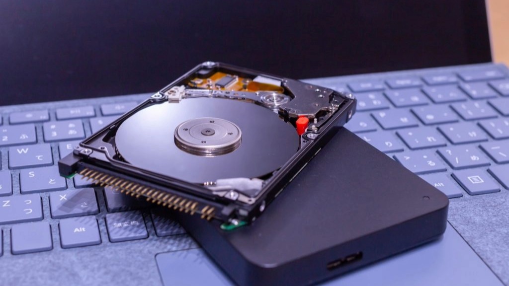 HDDデータ取り出しが必要な状況。ハードディスクと、データ復旧作業をイメージさせるノートパソコンDDデータ取り出しが必要な故障状況。分解され内部のプラッタが露出したハードディスクと、データ復旧作業をイメージさせるノートパソコン