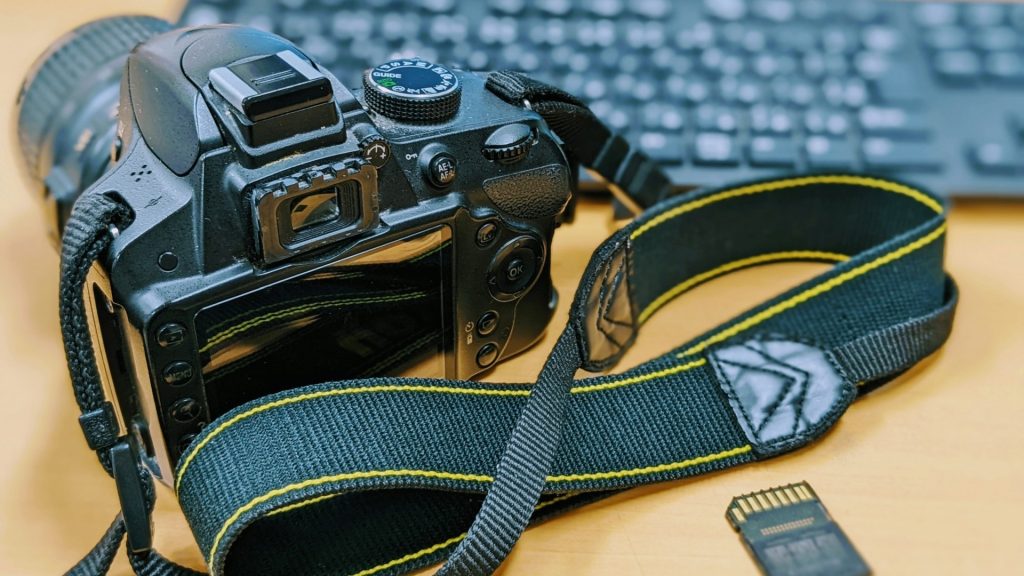 デスクの上に置かれたデジタルカメラと取り出されたSDカード、背景にパソコンのキーボードがある様子