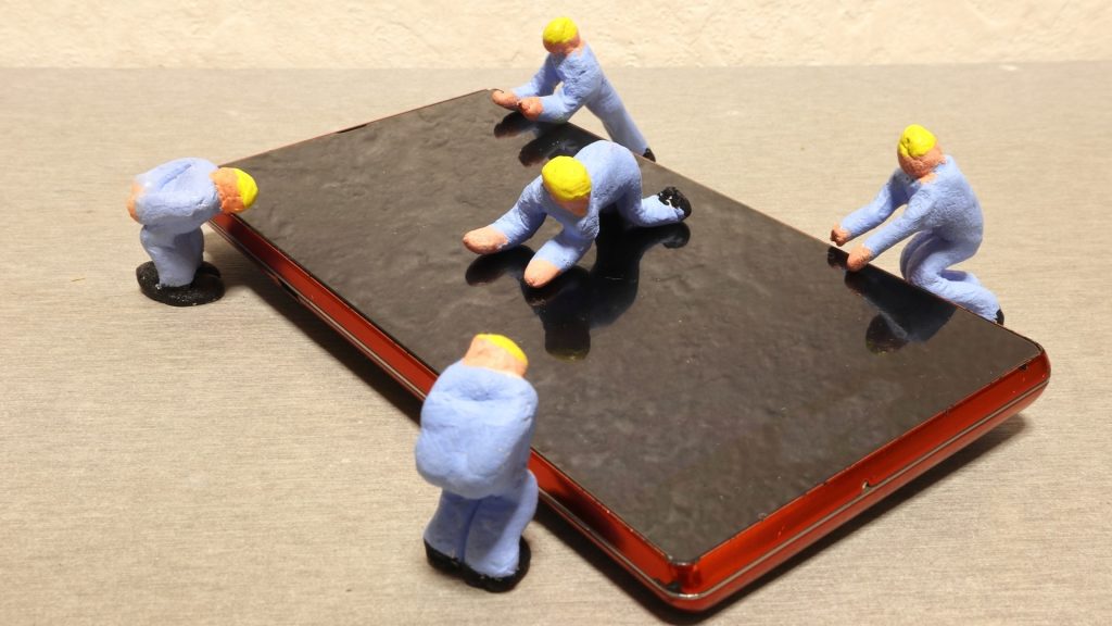 iPhoneのトラブルを解決するデータ復旧作業をイメージした、小さな作業員たちがスマートフォンをメンテナンスしている様子。