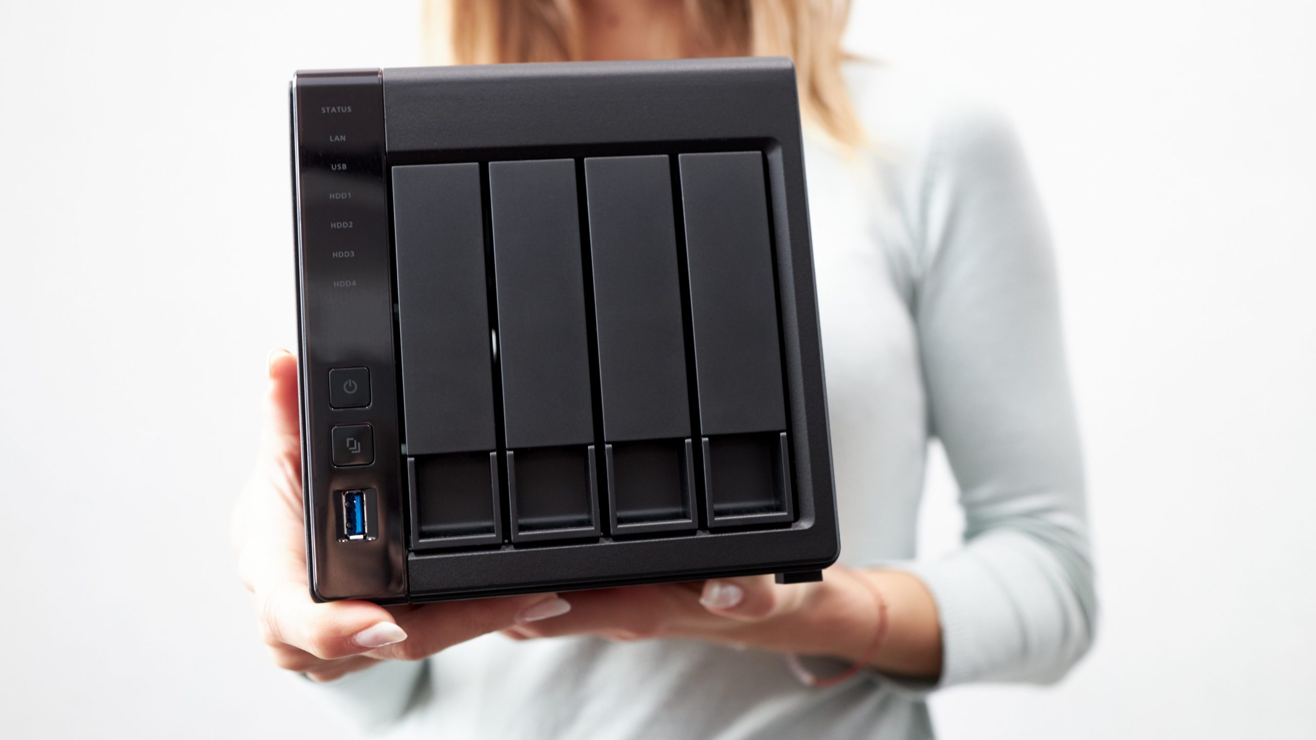 自力でNASのデータ復旧を行う方法を検討するため、女性が手に持つ4ベイタイプのNAS本体