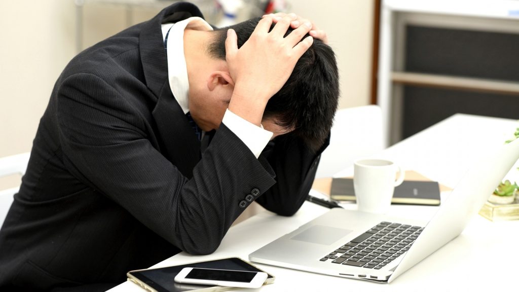 Windowsの自動修復が終わらないトラブルに直面し、頭を抱えて困るビジネスパーソン。パソコン故障や起動不可時の悩みのイメージ。