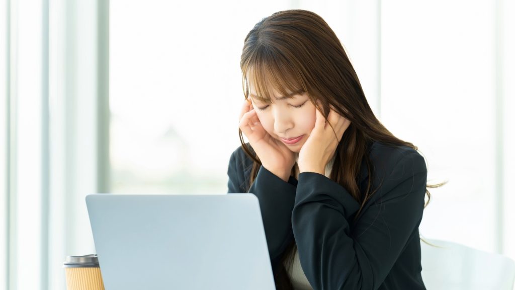 HDDの故障に対してチェックディスク(chkdsk)を安易に実行することで状況が悪化し、ノートパソコンの前で頭を抱えて深刻に悩み、困り果てているビジネスパーソンの女性。