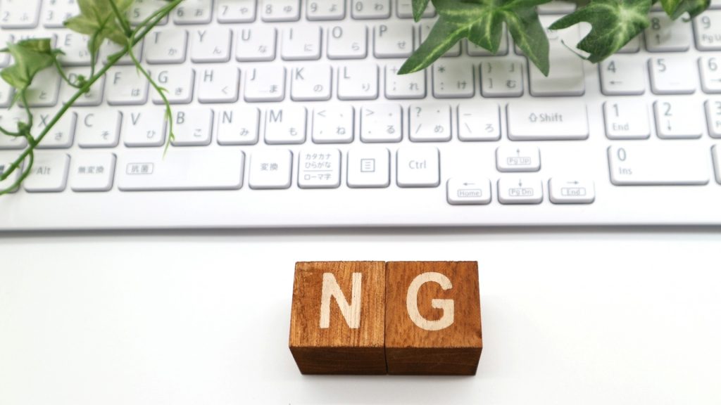 自動修復が終わらない時にやってはいけないNG行動を解説。清潔感のある白いキーボードの手前に置かれた、NGと刻印された木製ブロック。