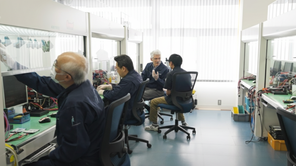 サーバー復旧業者のクリーンルームにて、制服を着た技術者がクリーンベンチを使用し、ハードディスクなどの精密なデータ復旧作業を行っている様子。